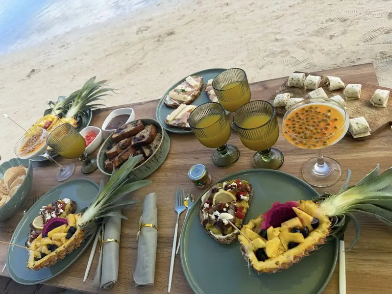 Brunch d'anniversaire dressé sur une plage du nord de l'Île Maurice avec toasts, fruits frais et jus